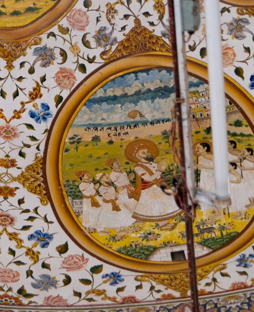 The first oval painting (in clockwise order) in the lower/outer circle in the ceiling of the mandapa (pillared hall) is the depiction of the meeting between Jain Acharya (those who impart knowledge), Shri Jinachadra Suri and the Mughal Emperor Akbar. He was invited to the Mughal court through Akbar’s court official Karamchand Bacchawat, who was from Bikaner. The painting has havelis (mansions) in the background, and the two leaders greet each other at the forefront. It is also said that Karamchand went to receive Jinachandra Suri on the outskirts of the city. The inscription reads, ‘Shri Jinadatta Suriji Akbar Badshah.’