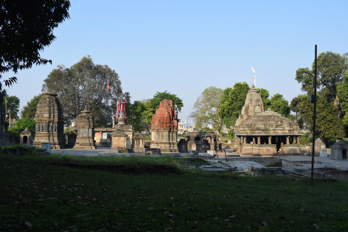 An overview of the Hanuman Garhi Temple complex from the eastern side. Seen here (from left to right) are many Shiva temples, behind it is the Hanuman Temple with a flag, Kumbheshwar Temple and Nilkhanth Mahadev Temple with the Surya Kund in front of it.