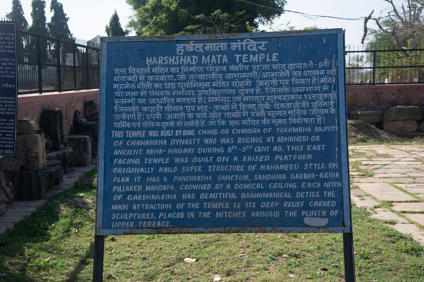 Information board in the temple premises installed by the Archaeological Survey of India (ASI) written in Hindi and English. The board provides information about the Harshat Mata Temple site and gives a basic introduction to the style of temple construction.