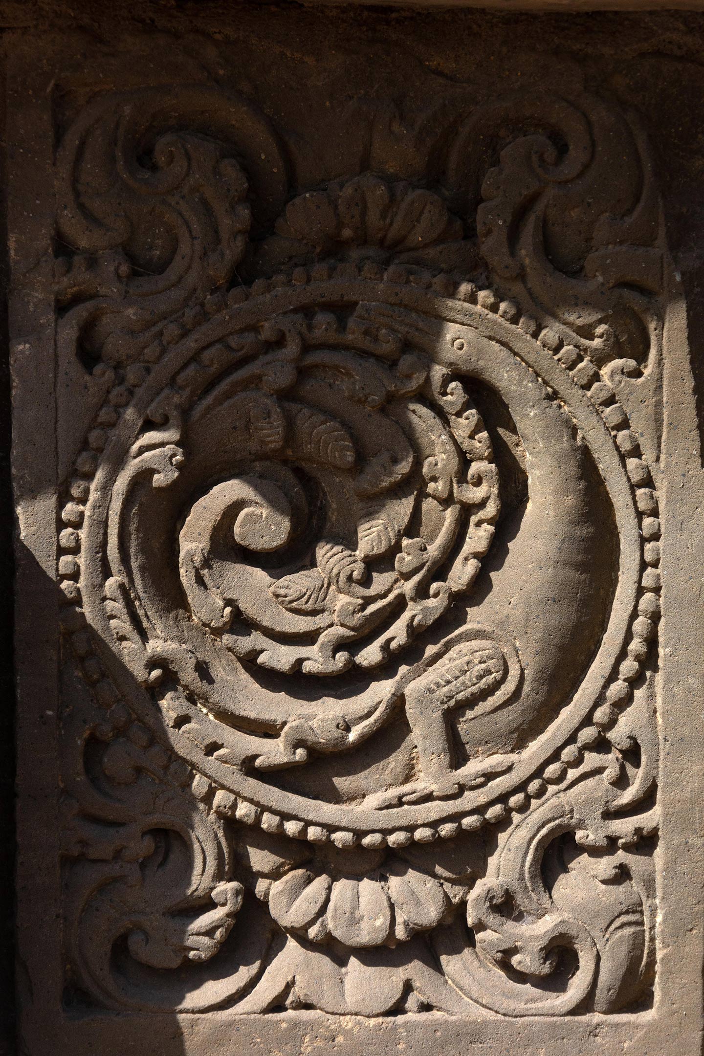 The central artwork of the plaque is in the form of a circular medallion surrounded by a foliage motif. Seen here is a floriated makara with its neck stretched around the medallion and the rear part integrated with flowing creeper motifs. The rest of the plaque is decorated with ardha padma (half lotus) and kalpa lata (creeper) motifs.
