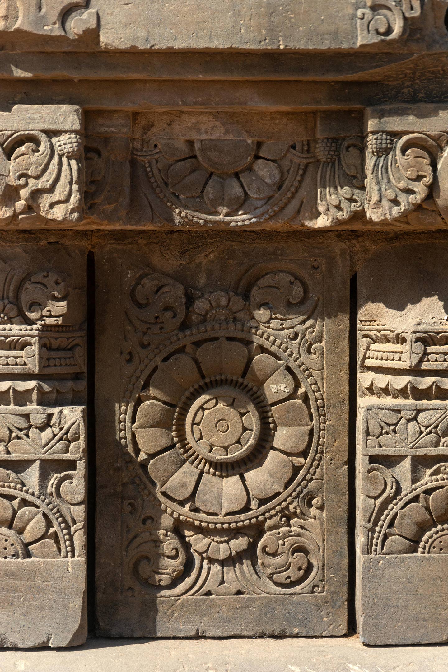 The plaque here features the ashtadal kamal (lotus with eight petals). The plaques are separated by squat pillars which have a square base, an octagonal shaft, and a square capital. The pillars are decorated with ardha padma (half lotus) and kalpa lata (creeper) motifs.