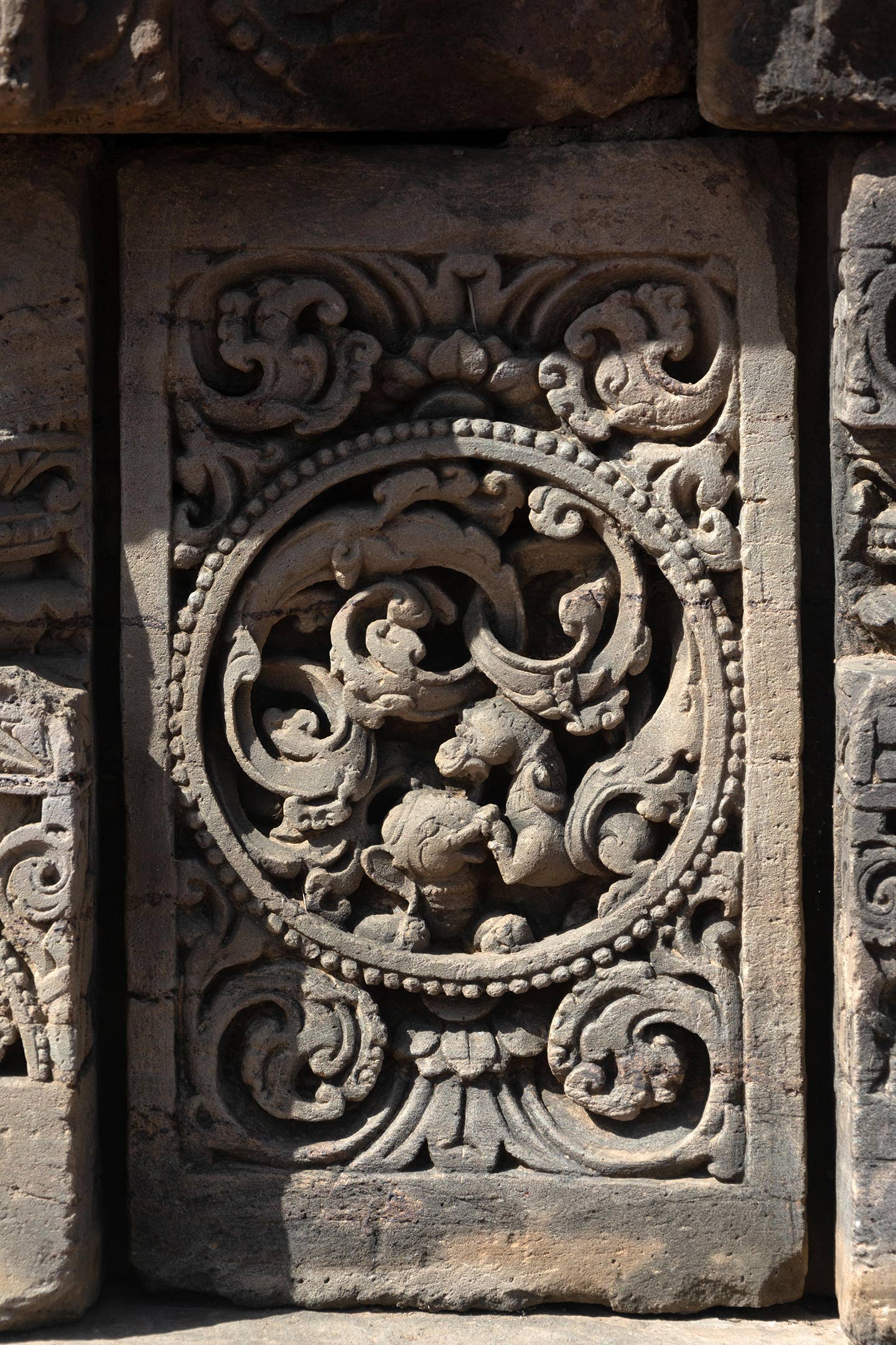 The central artwork of the plaque is in the form of a circular medallion surrounded by a foliage motif. Seen in this plaque, simha (lion) vyala and gaja (elephant) vyala engaged in a fight. The rest of the plaque is decorated with ardha padma (half lotus) and kalpa lata (creeper) motifs.