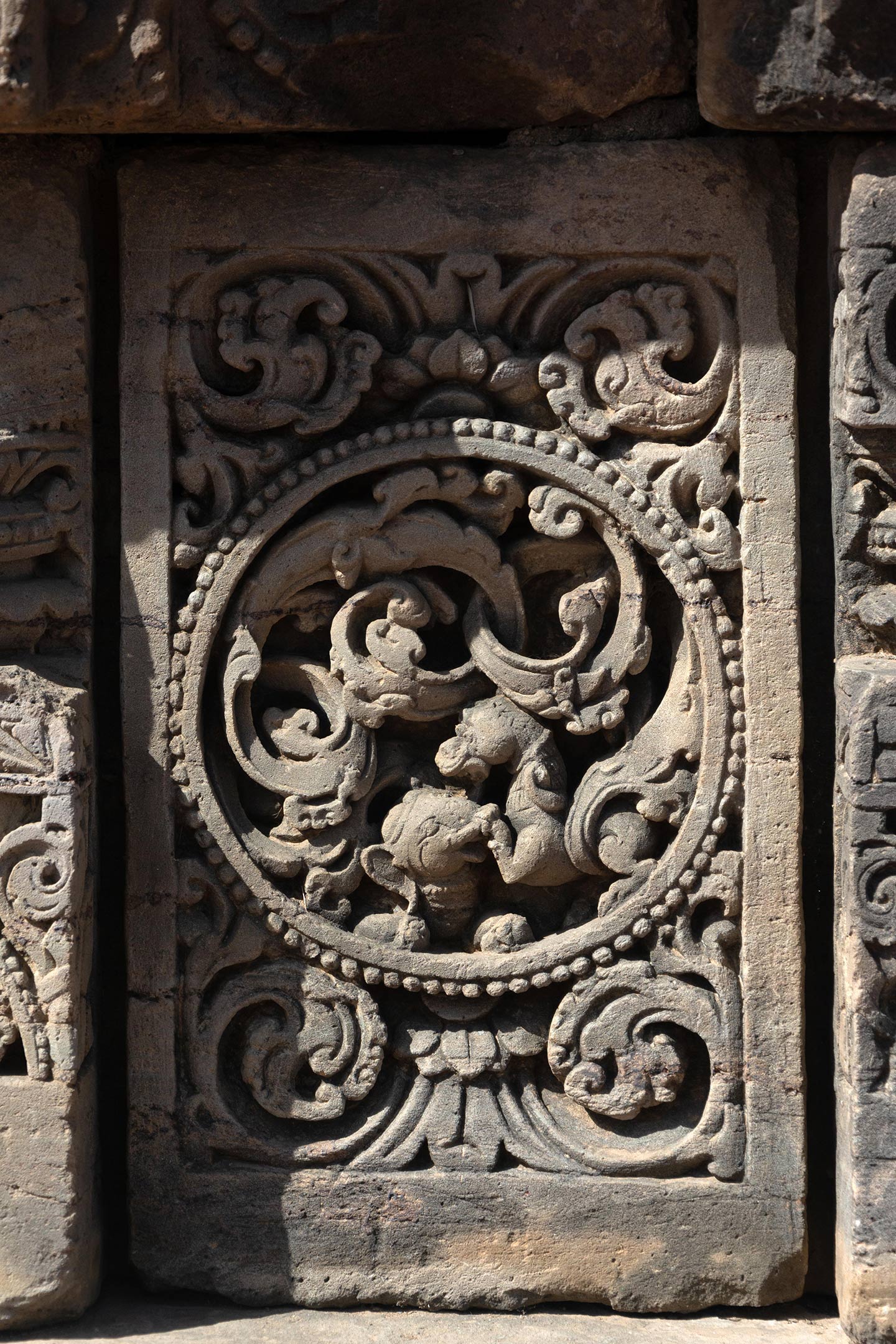 The plaque's central artwork takes the form of a circular medallion, encircled by a foliage motif. On this plaque, Simha (lion), and Gaja (elephant) Vyala are seen fighting. The rest of the plaque is decorated with ardha padma (half lotus) and kalpa lata (creeper) motifs.