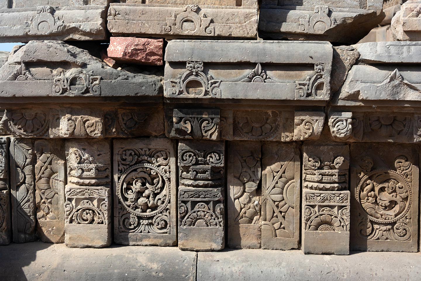 The plaque's central artwork consists of a circular medallion surrounded by a foliage motif. The left plaque features simha (lion) vyala and gaja (elephant) vyala engaged in a fight. The right plaque features a stylised makara. Squat pillars, characterized by a square base, an octagonal shaft, and a square capital, divide the plaques. The pillars are decorated with ardha padma (half lotus) and kalpa lata (creeper) motifs.