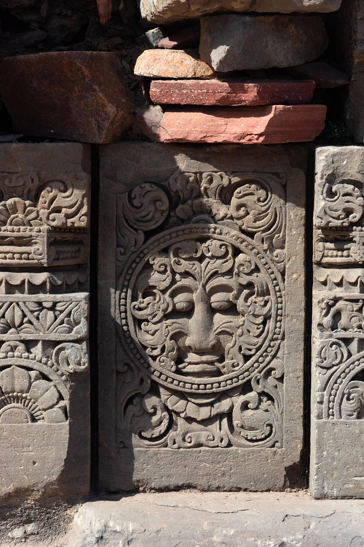 The medallion in the centre of the plaque has a kirtimukha (face of glory). The rest of the plaque surface is decorated with ardha padma (half lotus) and kalpa lata (creeper) motifs.