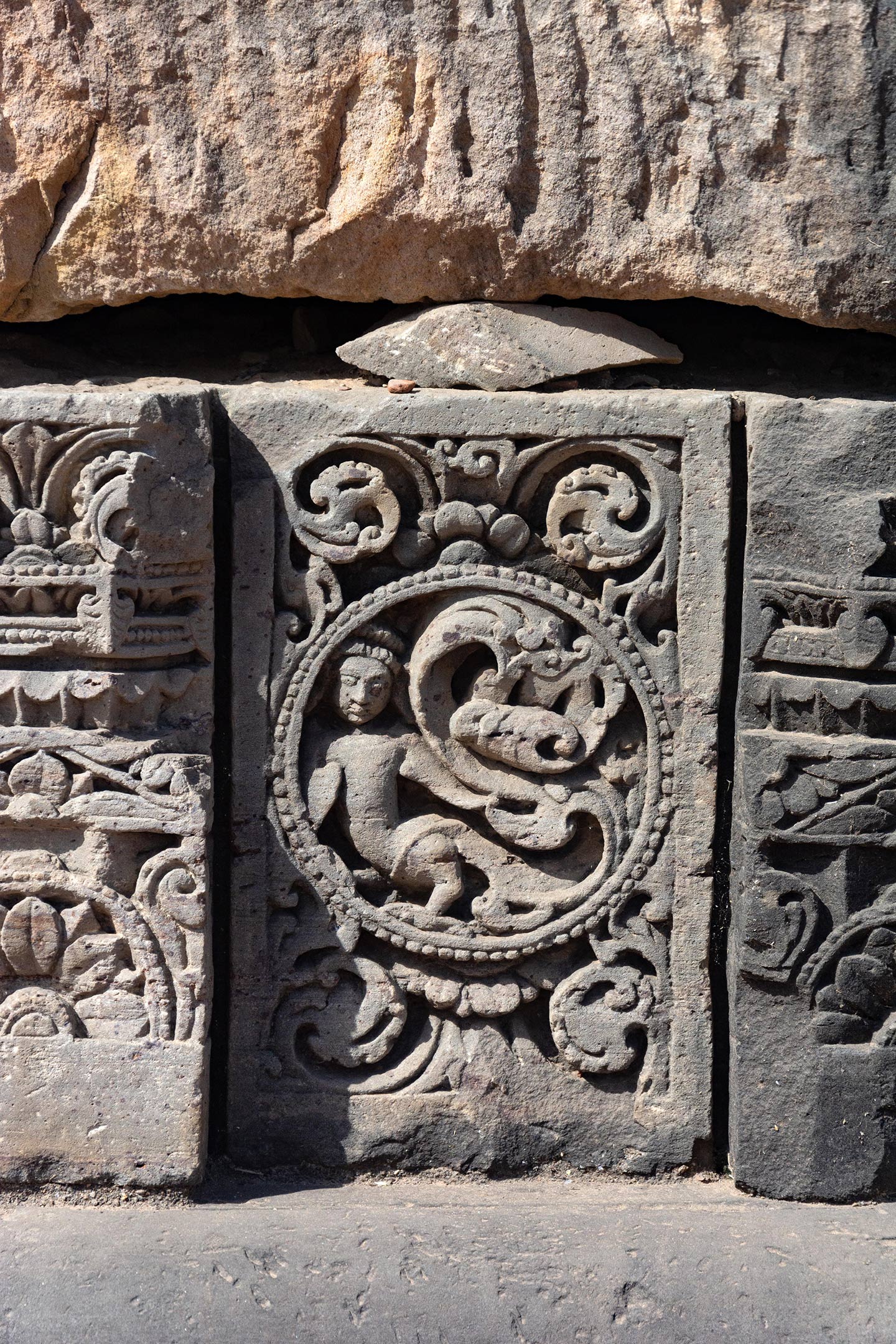 The medallion shows a kinnara (having the upper body of a human male and the lower body of a bird) with its tail forming a creeper motif. Kinnaras and kinnaris (having the upper body of a human female) are divine musicians who are skilled in dance, music, and poetry. The rest of the plaque surface is decorated with ardha padma (half lotus) and kalpa lata (creeper) motifs.