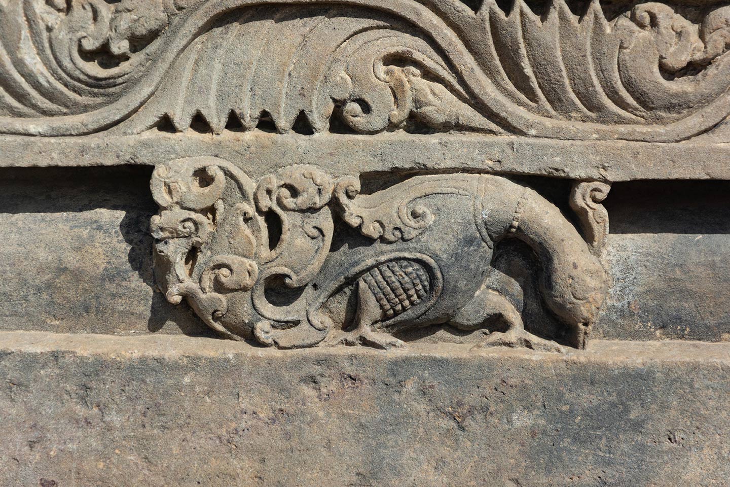 Bas relief of a peacock picking the food from the ground. A ring is placed on the neck of the bird.