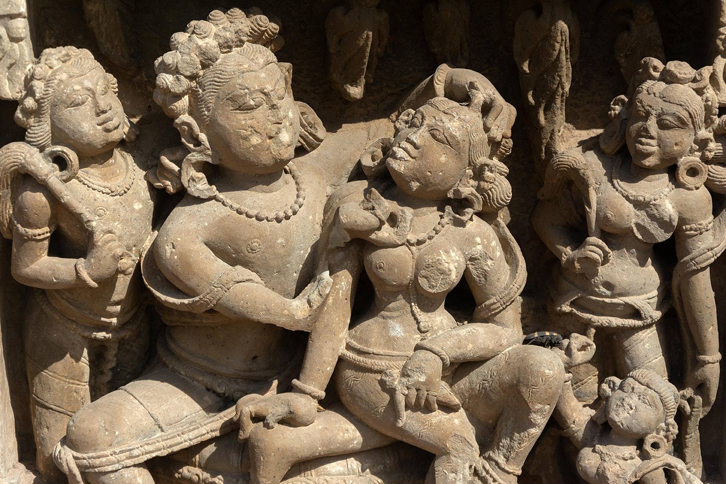 The man is admiring the beauty of the woman, placing his left hand on her coiffure and inspecting her face with his left hand (missing). Chauri dharini (fly whisk bearers) stand on either side of the couple, looking towards them. A small female figure features at the right bottom, likely an attendant or servant.