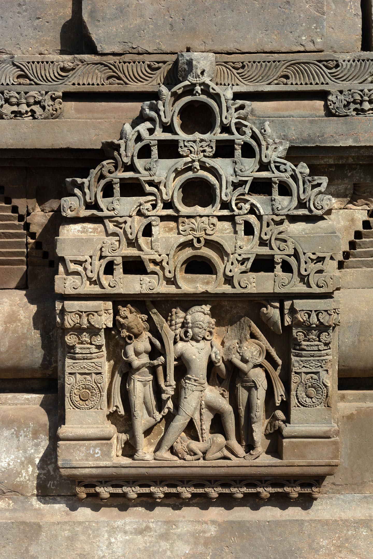 This panel depicts a warrior invoking raudram rasa (fury/rage) by aggressively wielding a drawn sword. The central figure of a warrior-king is aggressively stepping forward wielding a naked sword in his right hand. A dagger is tucked into his kamarbandha (waist belt). The central female figure (seen on the left) may be a queen, who is trying to stop the man by pulling him behind.