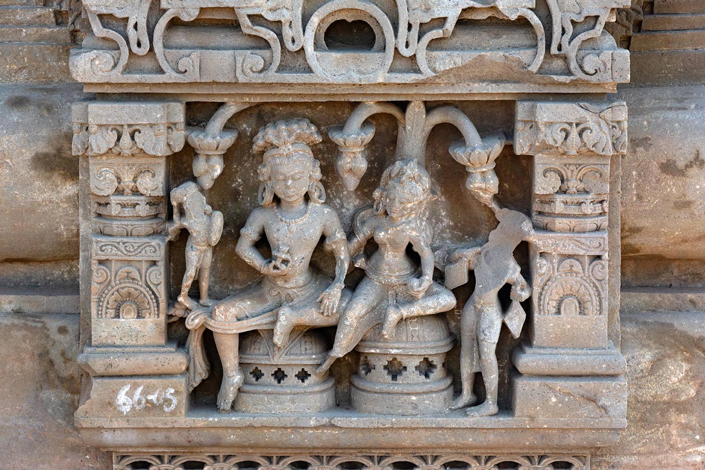 The male figure in the center holds a flower in his right hand, while his left hand rests on his leg. The central female figure carries a round fruit (or sweet) in her left hand and holds the man's left hand with her right hand, showing affection. On either side, two attendants flank the couple. In the background, flowering trees droop.