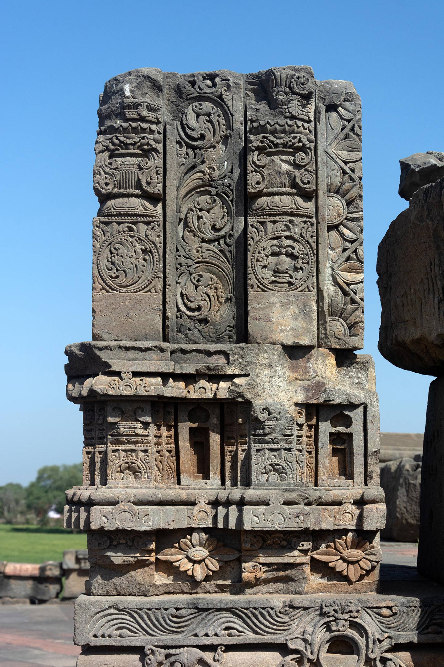 The upper block has the kalpavrisksha (tree of life) motif running along a central band. Damaged panels on either side display prominent features such as the kalpa lata (creeper) motif (bottom left), the purna ghata (overflowing pot of prosperity) motif (mid-sections), and the kirtimukha motif (bottom right). The block in the middle has the ardha padma (half lotus) motif.