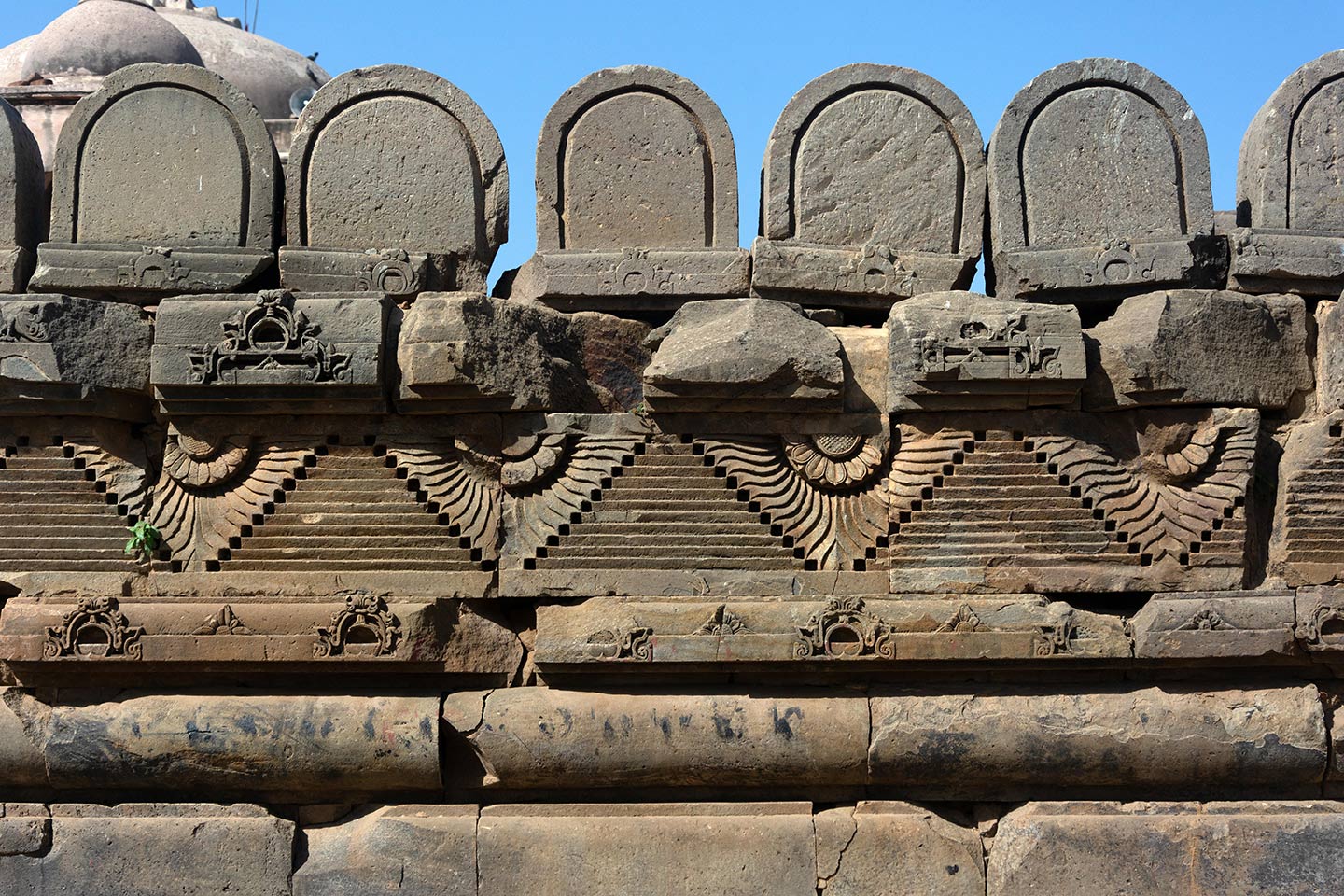 Image 2: Broken debris from the original temple assembled on the southeast face of the adhisthana (elevation of the first tier). U-shaped rounded stones are assembled on the parapet (their position or purpose in the original temple is unknown). Relief carvings of geometric, flora, and fauna motifs feature all around the adhisthana.