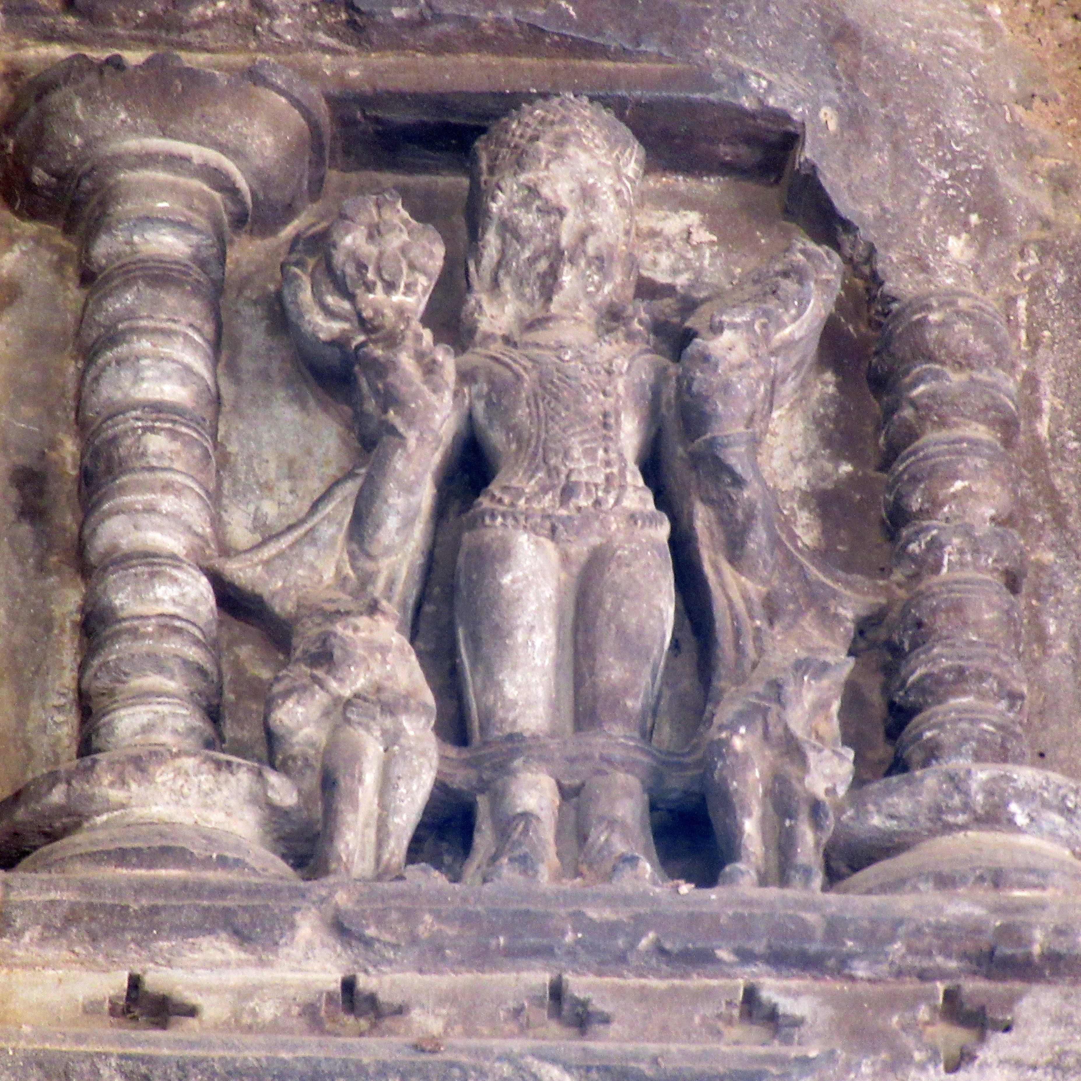 Image 10: Standing male deity in the samabhanga pose adorned with a mukuta (headgear), meshed armour, uttariya (stole or scarf-like garment), and boots. In both hands, he holds lotuses in full bloom. Broken figures of Danda and Pingala are present on either side of the legs.