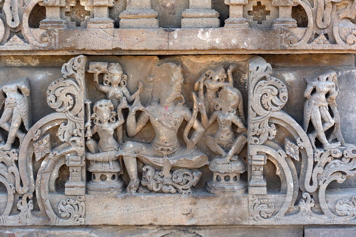 Image 17: This panel depicts Varuna, a Vedic deity. Varuna is both the god of oceans and a dikpala (guardian of directions). Since Varuna is the guardian of the west, the west face of the adhisthana features his image. On the mythical sea creature known as Makara, Varuna sits in a lalitasana posture. Varuna holds the Gandiva, a divine bow, in his left hand, which Varuna gifted to Arjuna in the Mahabharata. Four female attendants surround him. Two attendants sit on circular seats in the foreground, while two stand in the background.